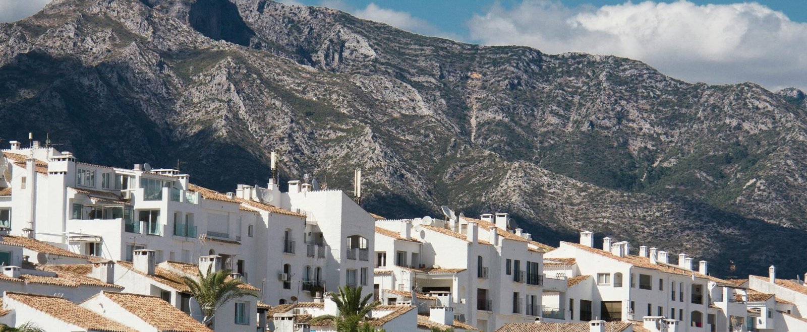Elegant yachts docked at a Mediterranean harbor with picturesque mountain and town backdrop.